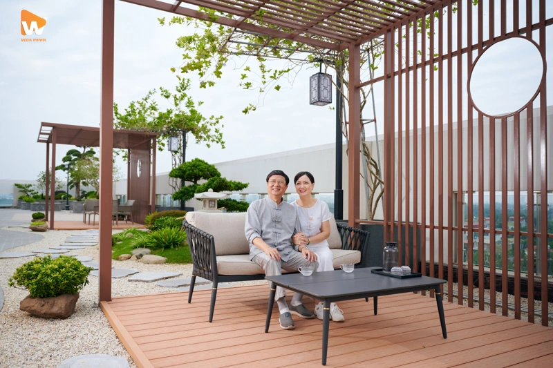 Cặp đôi đang vui vẻ trò chuyện và thưởng thức đồ uống tại tầng thượng khách sạn với view thành phố lung linh.
