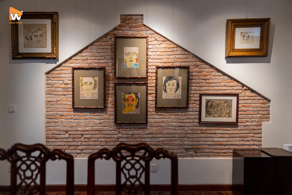 Một góc chụp ảnh đẹp và ấm cúng tại CAFE 36 Phố, với hai chiếc ghế gỗ cổ điển bên cạnh bức tường gạch mộc mạc và tranh treo tường.