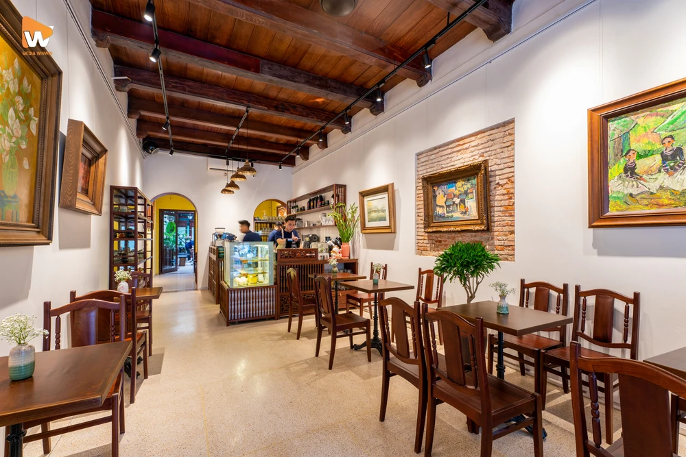 Chụp ảnh trong quán cafe 36 Phố với không gian phòng tranh nghệ thuật chủ đạo, nổi bật với bàn ghế gỗ và các tác phẩm hội họa